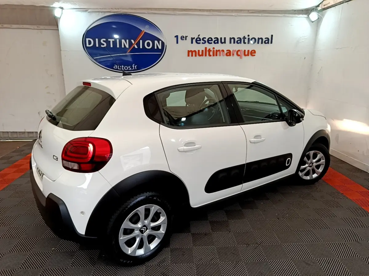 Vue 3/4 arrière droite d'une Citroën C3 blanche avec protections noires latérales et jantes argentées dans un garage.