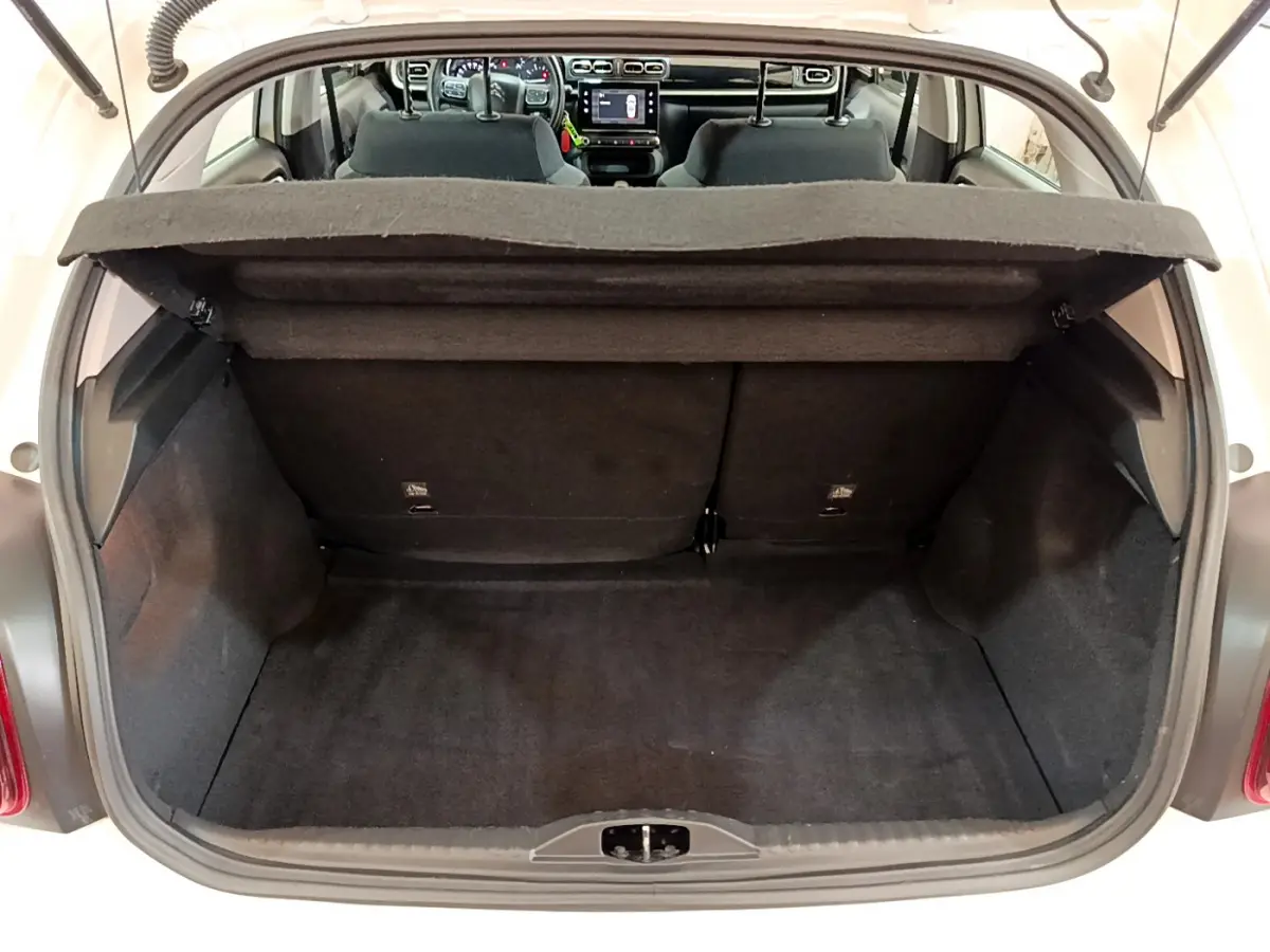 Coffre ouvert de la Citroën C3 blanche vue de l'arrière, avec intérieur noir et tableau de bord visible à travers le pare-brise.