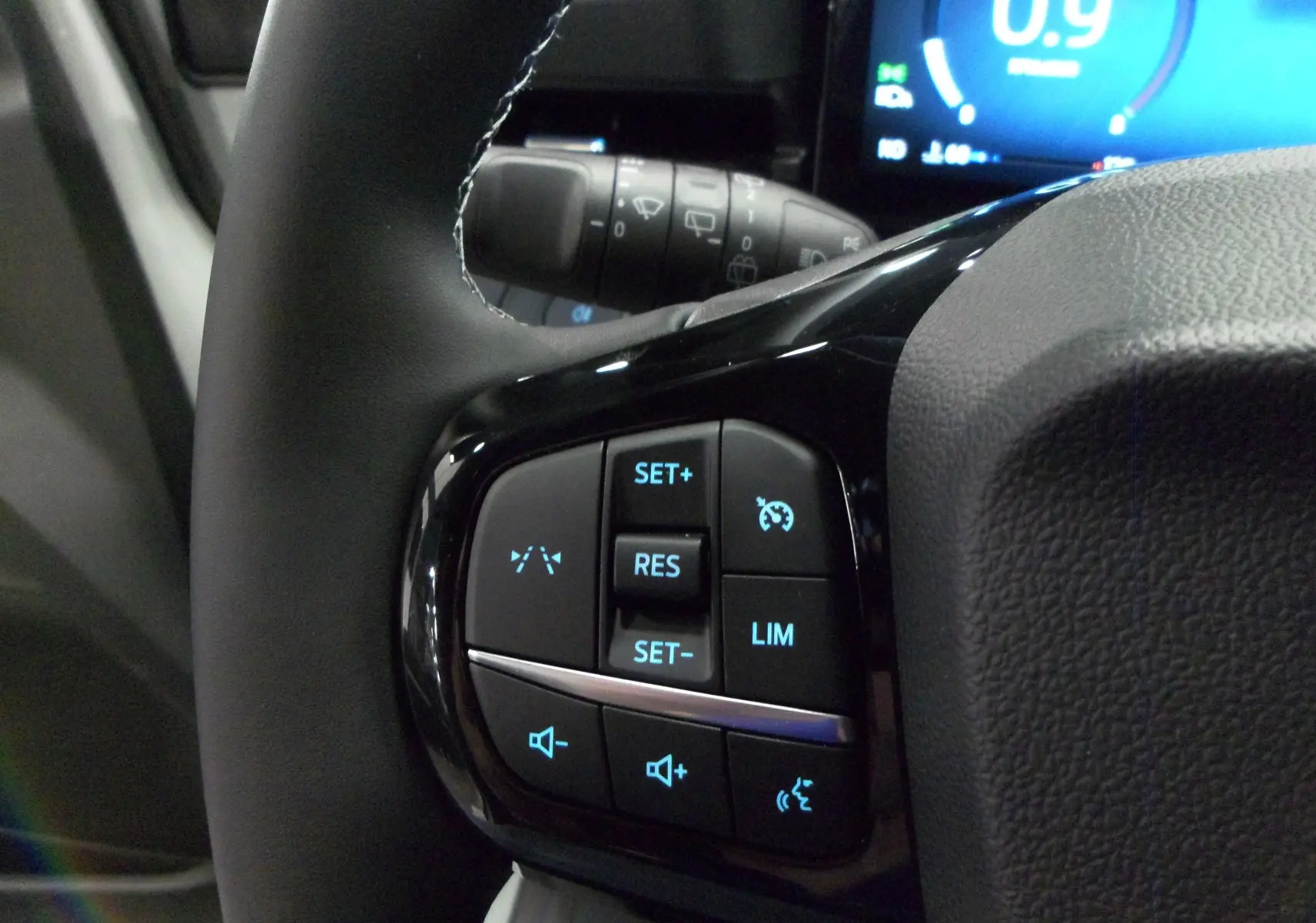 Gros plan sur les commandes au volant gauche du Ford Puma gris, avec régulateur de vitesse et contrôle audio rétroéclairés.