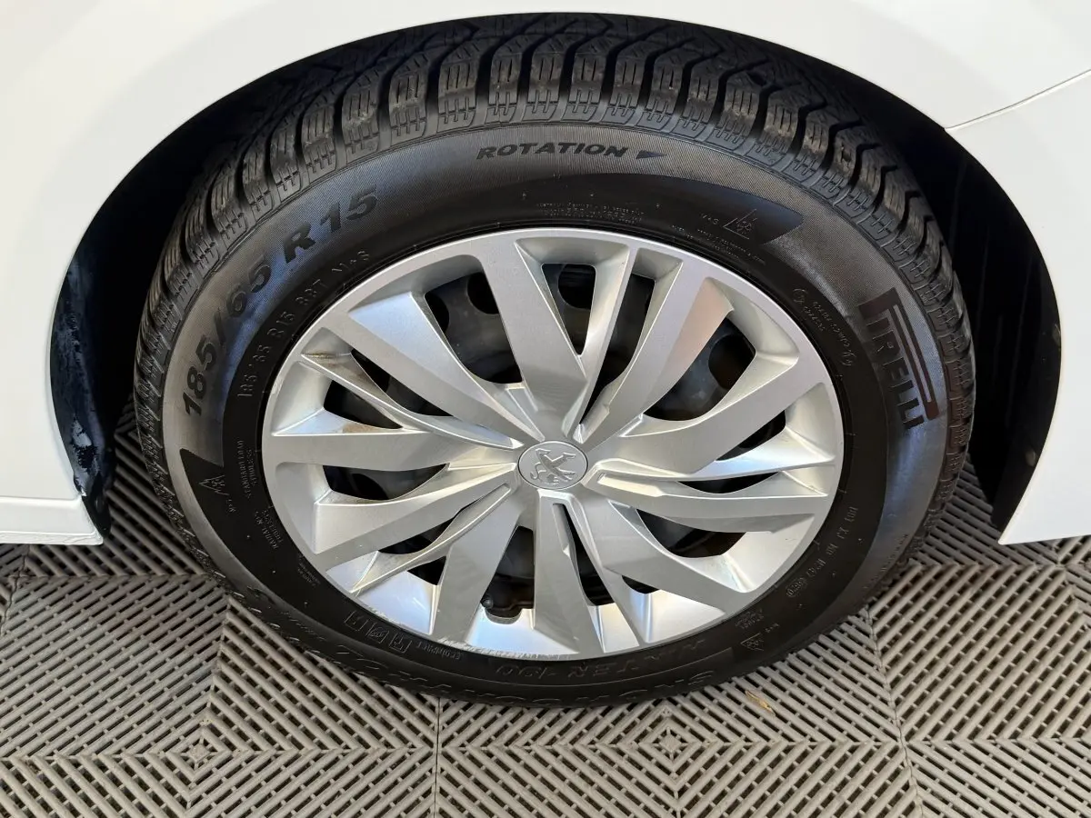 Gros plan sur la roue avant droite d'une Peugeot 208 blanche, avec jante argentée et pneu Pirelli visible.