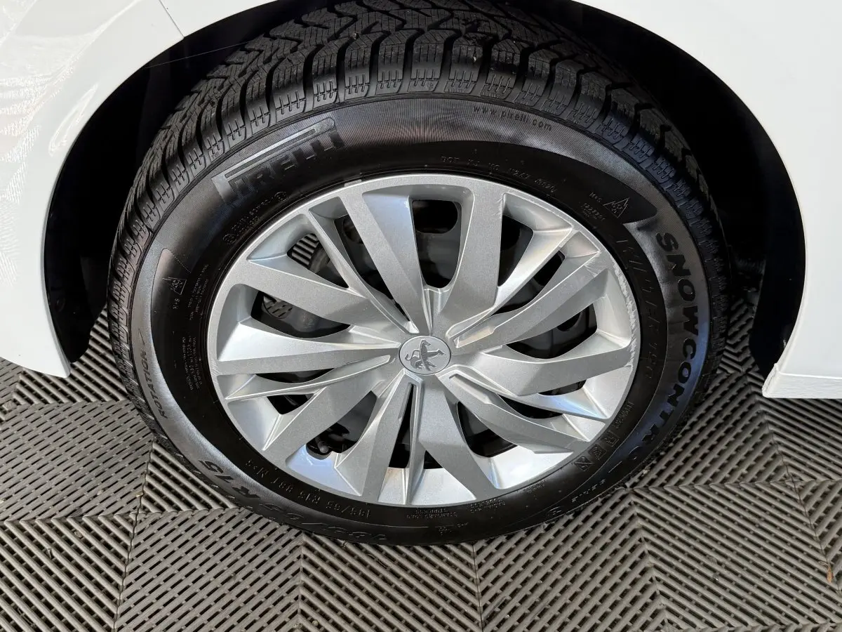 Gros plan sur la roue avant droite argentée d'une Peugeot 208 PureTech 75 S&S Like blanche, pneu hiver Pirelli.