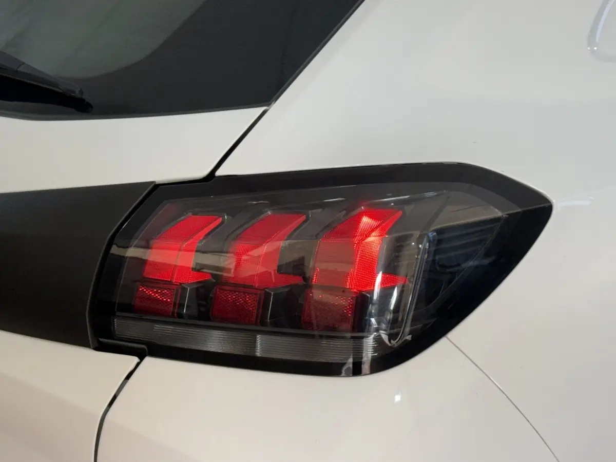 Gros plan sur le feu arrière droit noir et rouge d’une Peugeot 208 PureTech 75 S&S Like blanche.