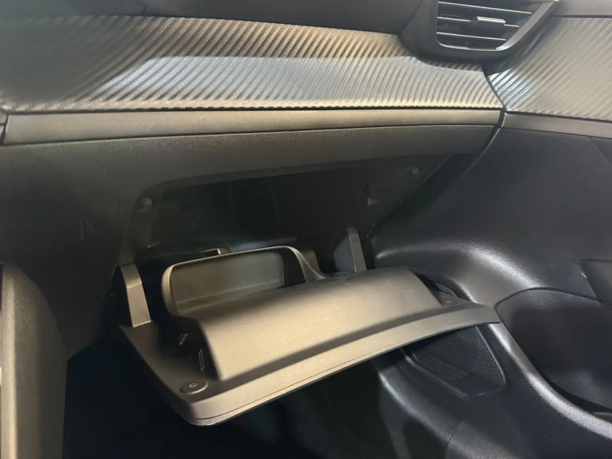 Intérieur de la Peugeot 208 PureTech 75 S&S Like 2020, vue sur la boîte à gants ouverte avec finition noire et effet carbone.