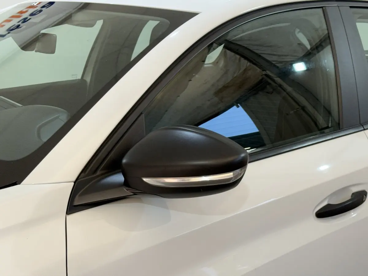 Vue rapprochée du côté gauche avant d'une Peugeot 208 PureTech 75 S&S Like blanche avec rétroviseur noir et clignotant intégré.