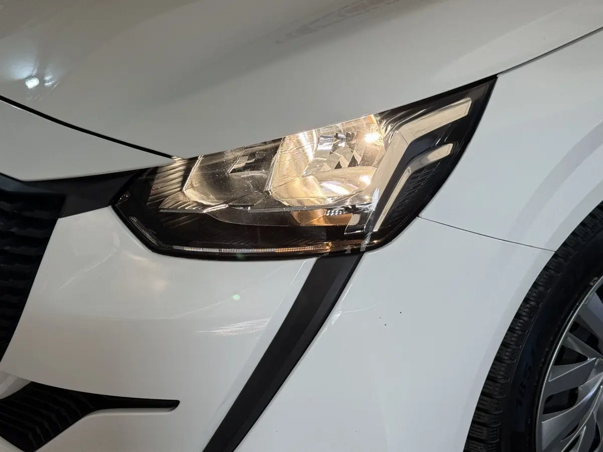 Gros plan sur le phare avant droit allumé d’une Peugeot 208 PureTech 75 S&S Like blanche de 2020.