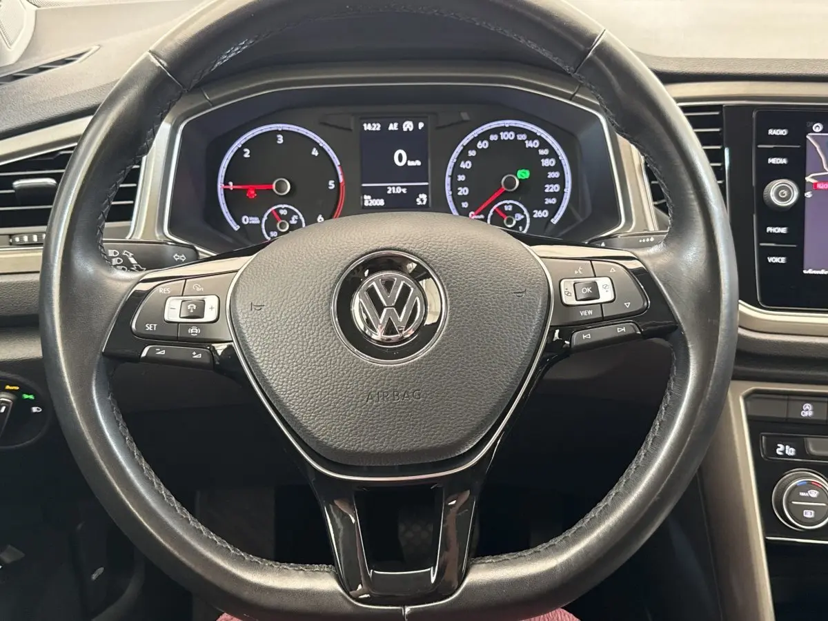 Vue rapprochée du volant cuir noir du Volkswagen T-Roc 2.0 TDI 150, avec tableau de bord numérique et commandes intégrées.