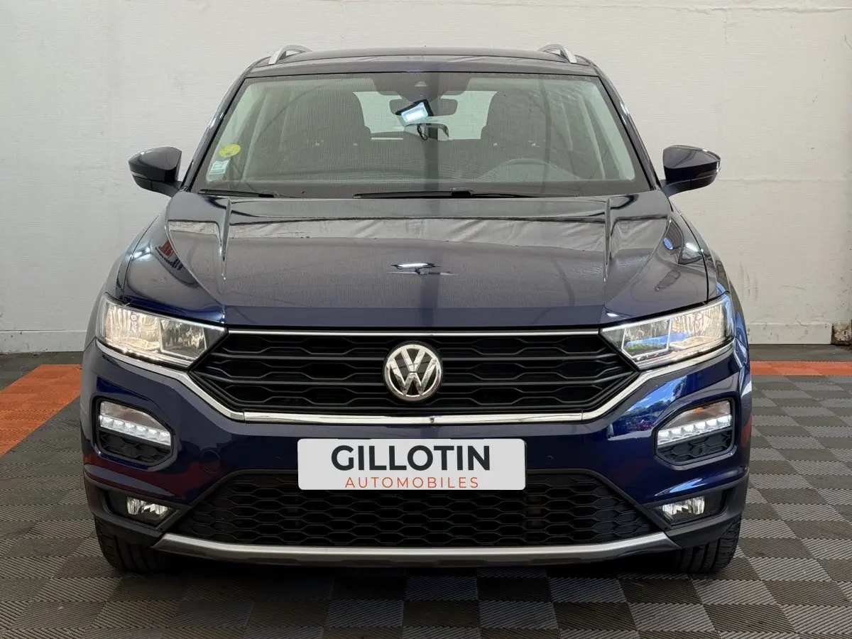 Vue avant d'un Volkswagen T-Roc bleu 2020 avec calandre noire et feux LED allumés sur fond intérieur neutre.