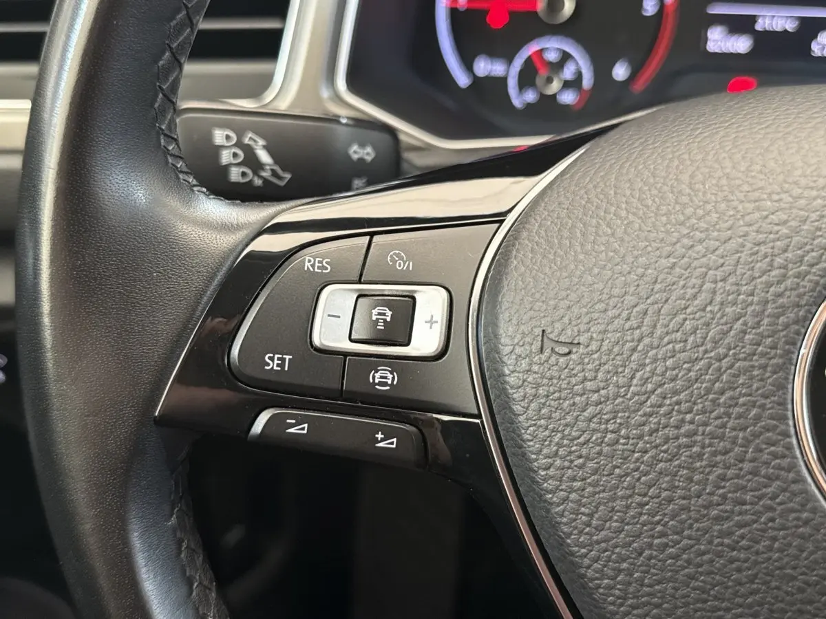 Gros plan sur les commandes du volant cuir noir du Volkswagen T-Roc 2.0 TDI, affichage digital en arrière-plan.