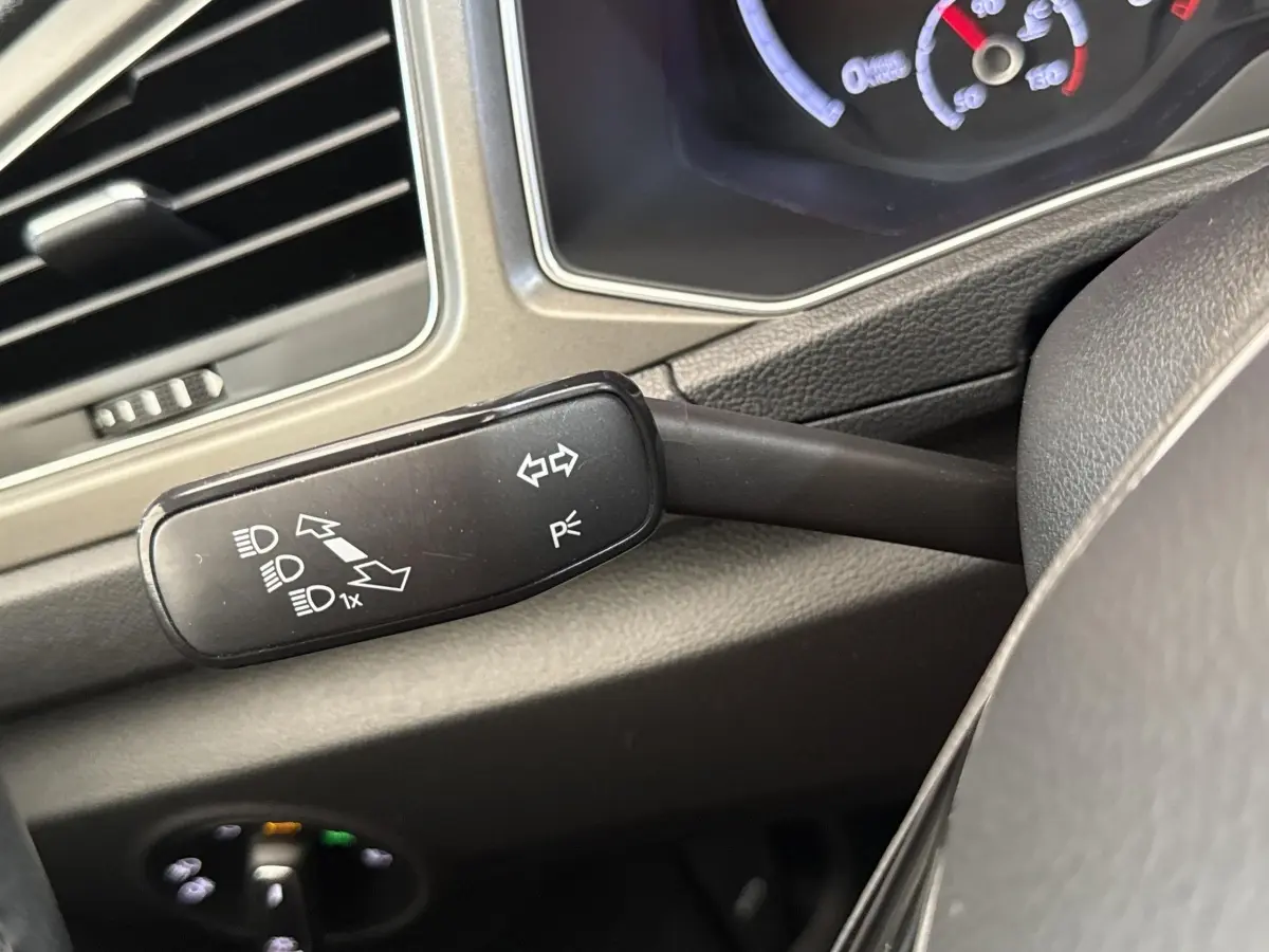 Gros plan sur la commande de clignotants et feux à gauche du volant dans l’habitacle du Volkswagen T-Roc bleu.