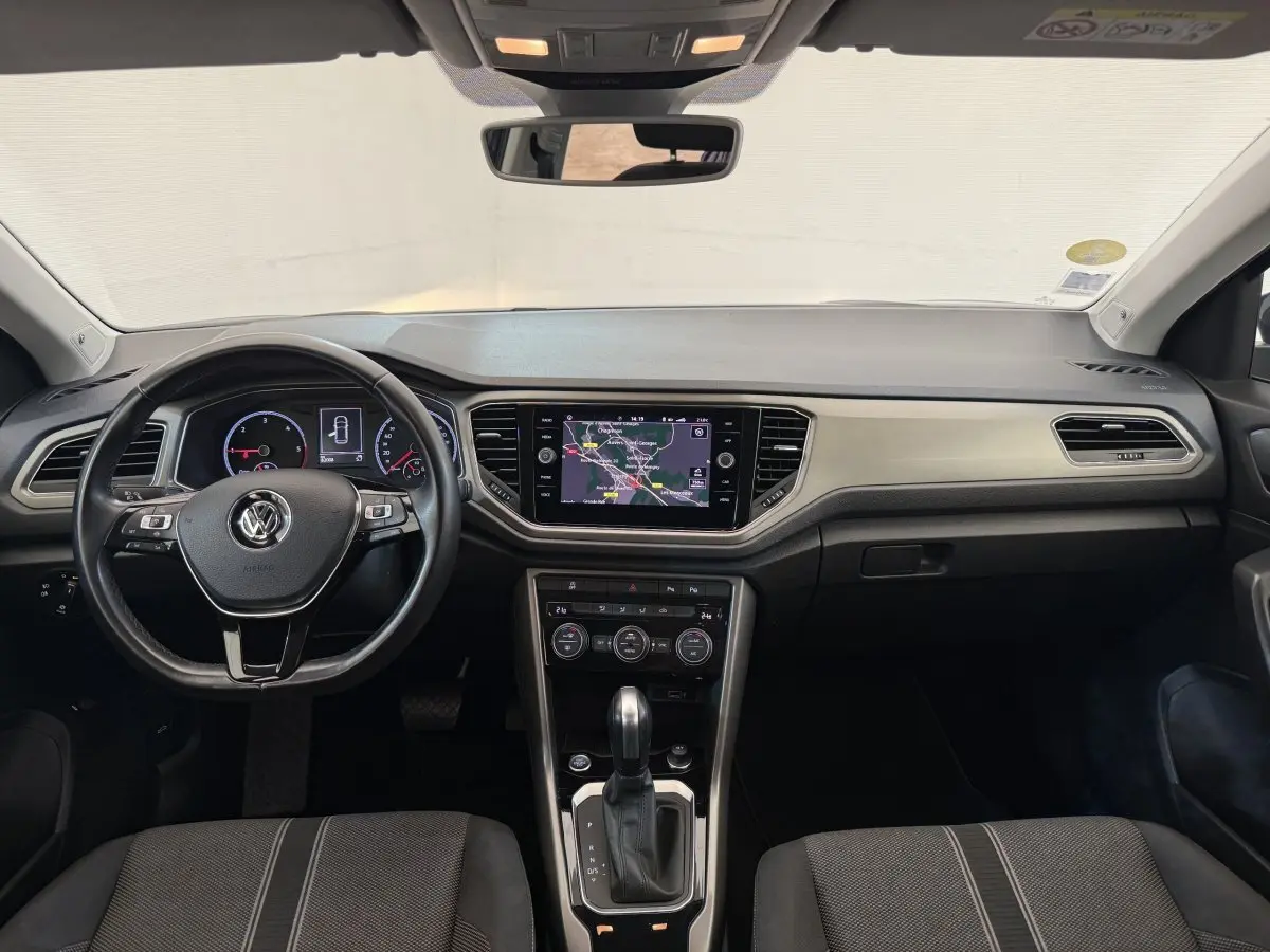 Vue frontale de l'habitacle du Volkswagen T-Roc bleu, avec tableau de bord numérique et écran tactile central.