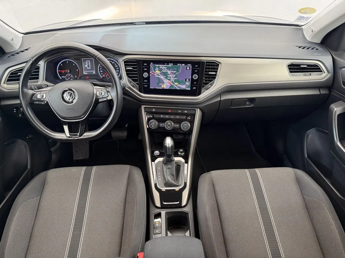 Vue intérieure avant du Volkswagen T-Roc 2.0 TDI bleu, montrant tableau de bord, volant cuir et écran tactile central.