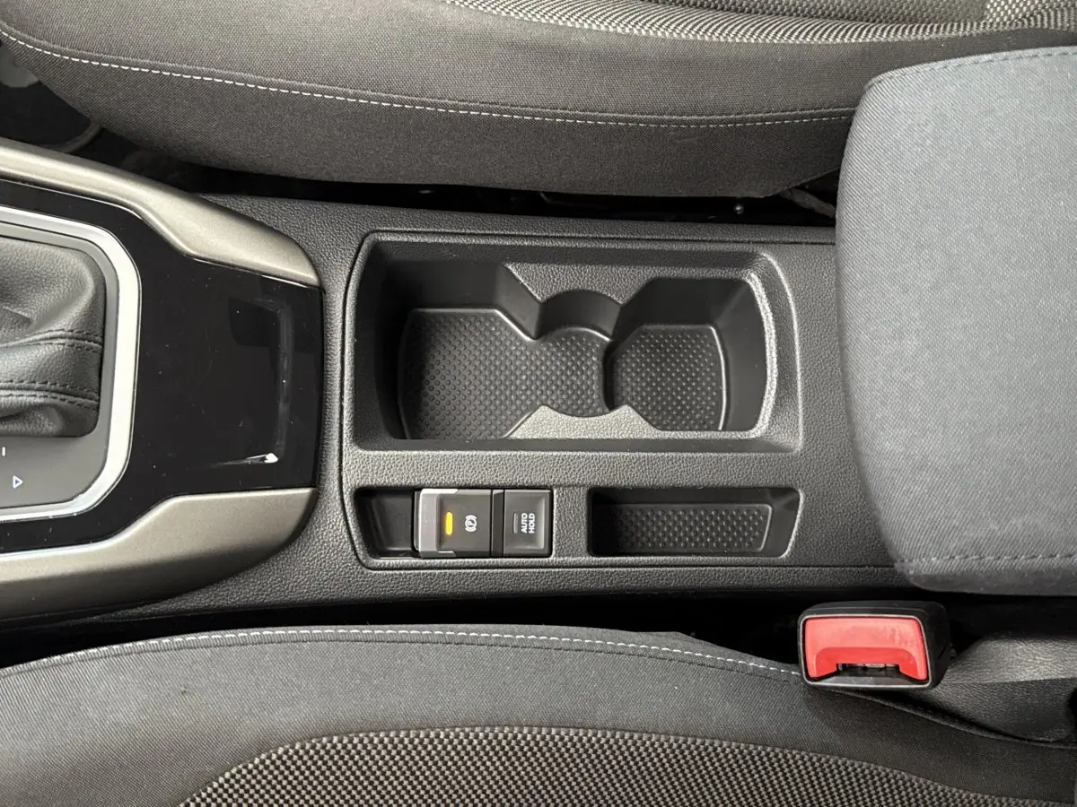 Vue plongeante sur la console centrale noire du Volkswagen T-Roc bleu, avec porte-gobelets et frein à main électrique.