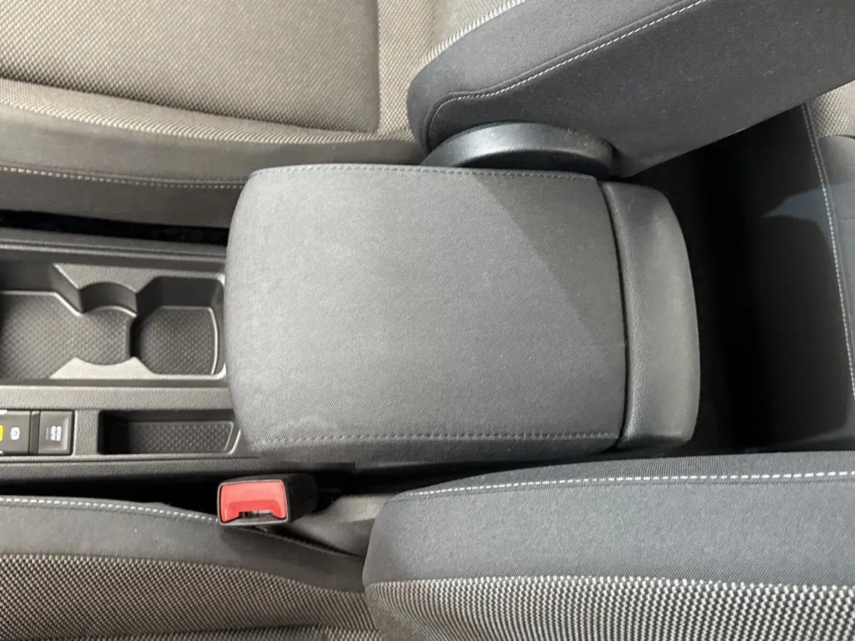 Vue rapprochée de l'accoudoir central et console noire du Volkswagen T-Roc bleu, avec bouton de frein à main électrique visible.