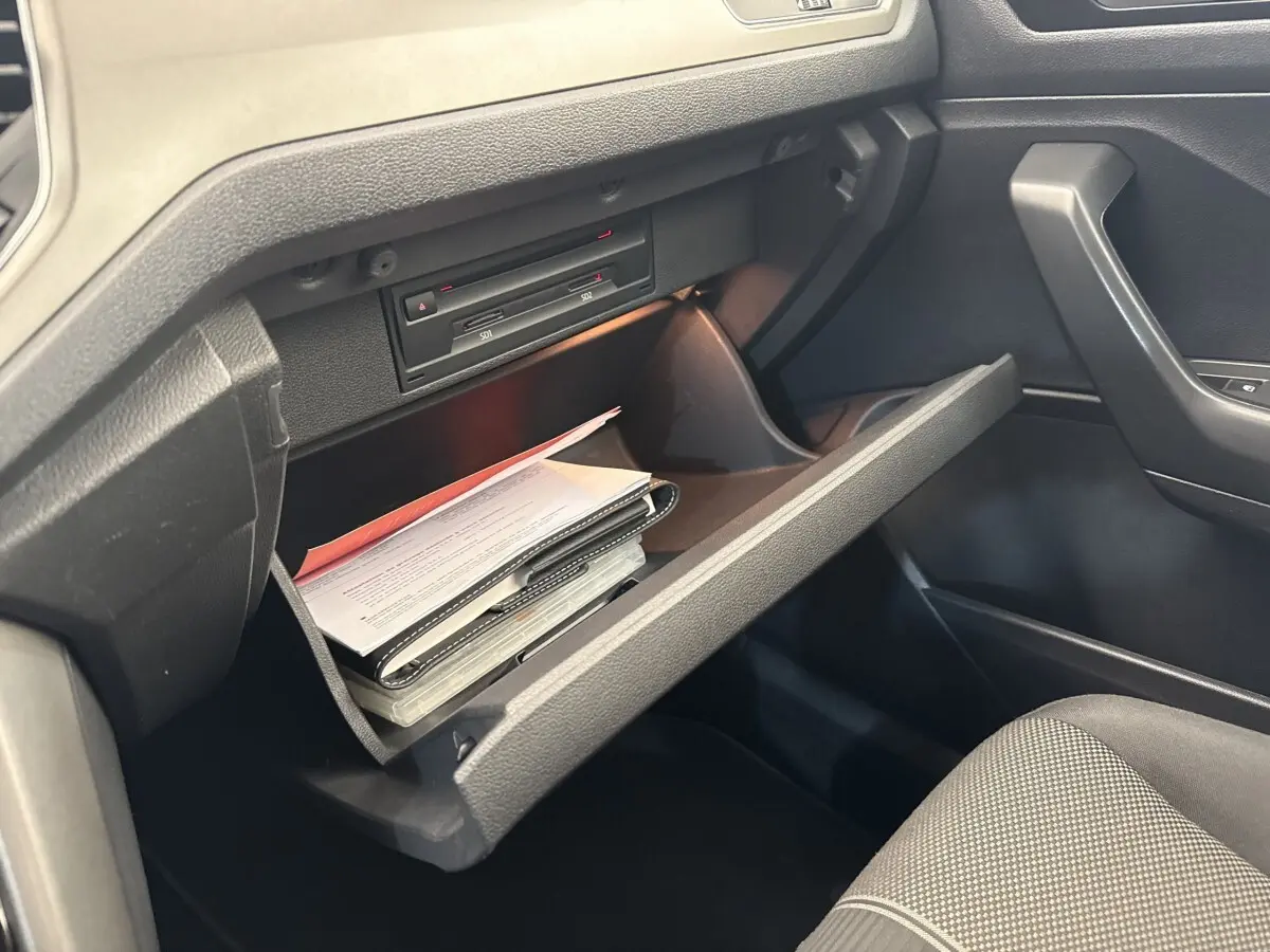 Vue intérieure du coffre à gants ouvert côté passager d'un Volkswagen T-Roc 2.0 TDI bleu, montrant des documents rangés.