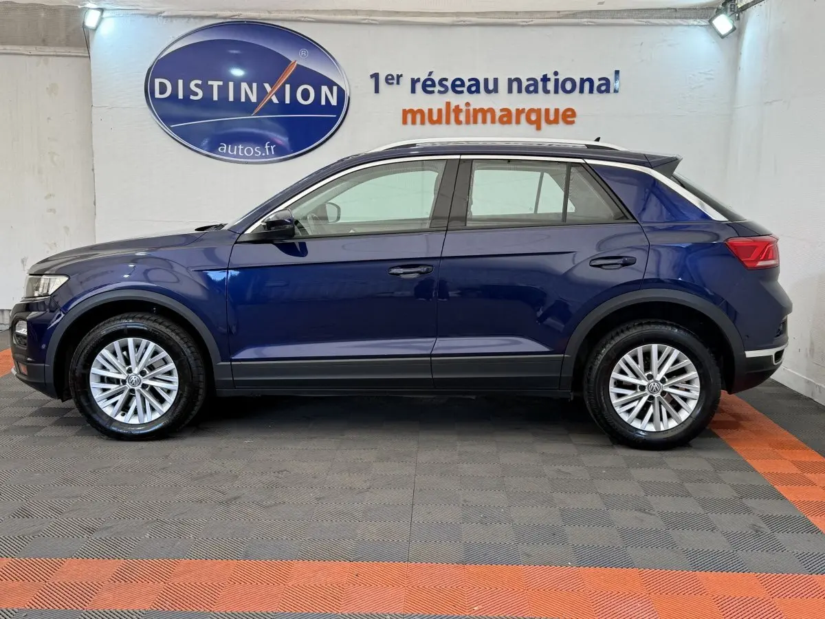 Vue latérale droite d'un Volkswagen T-Roc bleu 2020, avec jantes alliage et barres de toit noires visibles.