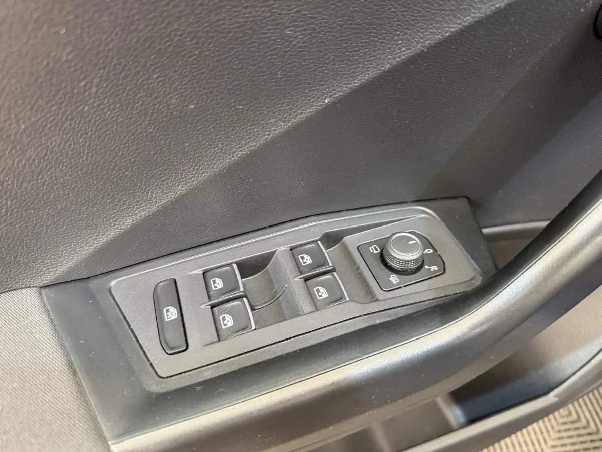 Gros plan sur les commandes électriques des vitres et rétroviseurs sur la porte avant gauche d’un Volkswagen T-Roc bleu.