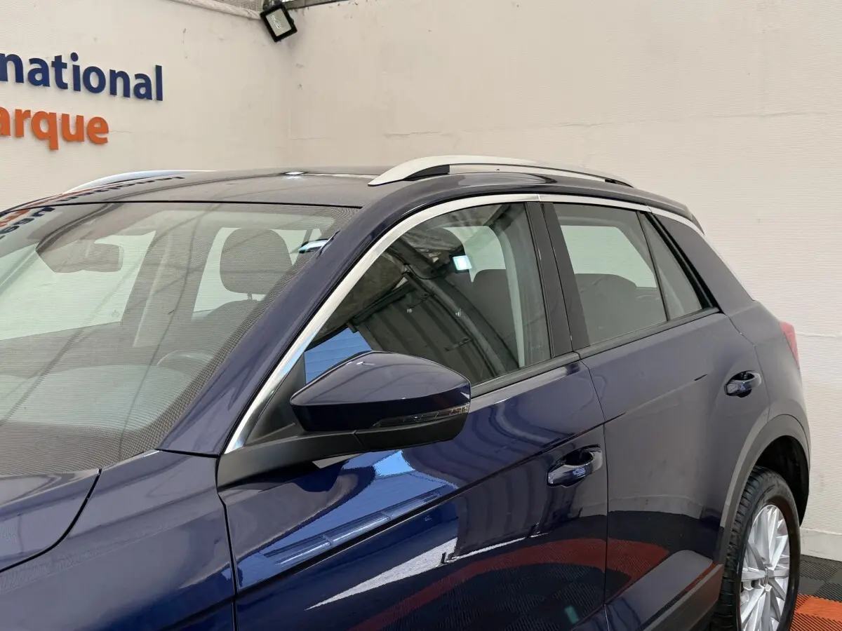 Vue latérale côté gauche d'un Volkswagen T-Roc bleu 2020 avec rétroviseurs et rails de toit visibles.