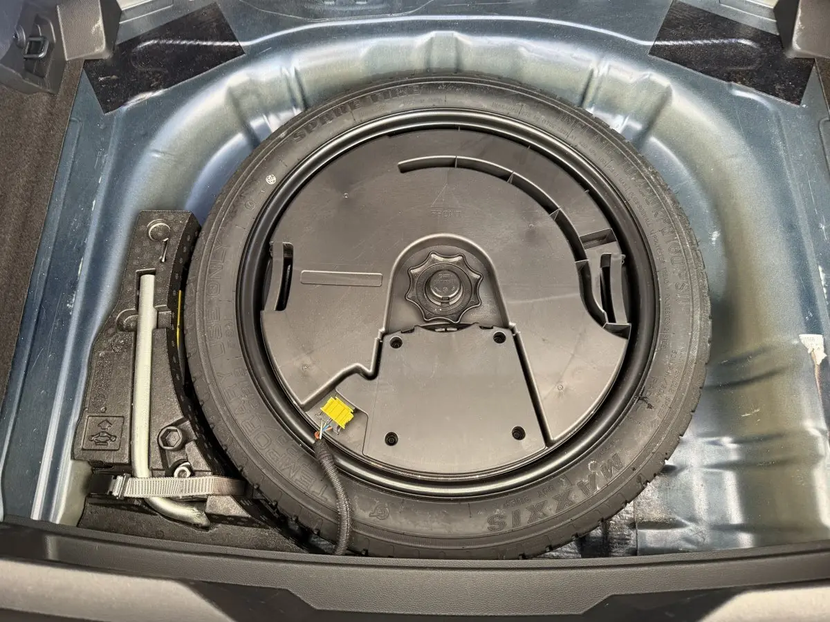 Vue plongeante sur la roue de secours et le cric dans le coffre d'un Volkswagen T-Roc bleu 2020.