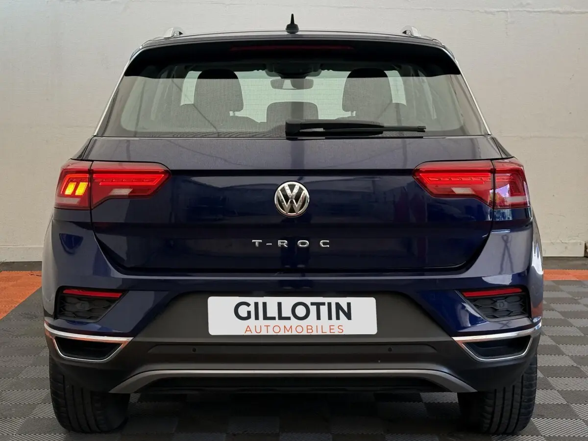 Vue arrière d'un Volkswagen T-Roc bleu 2020 avec feux LED allumés et logo VW bien visible.