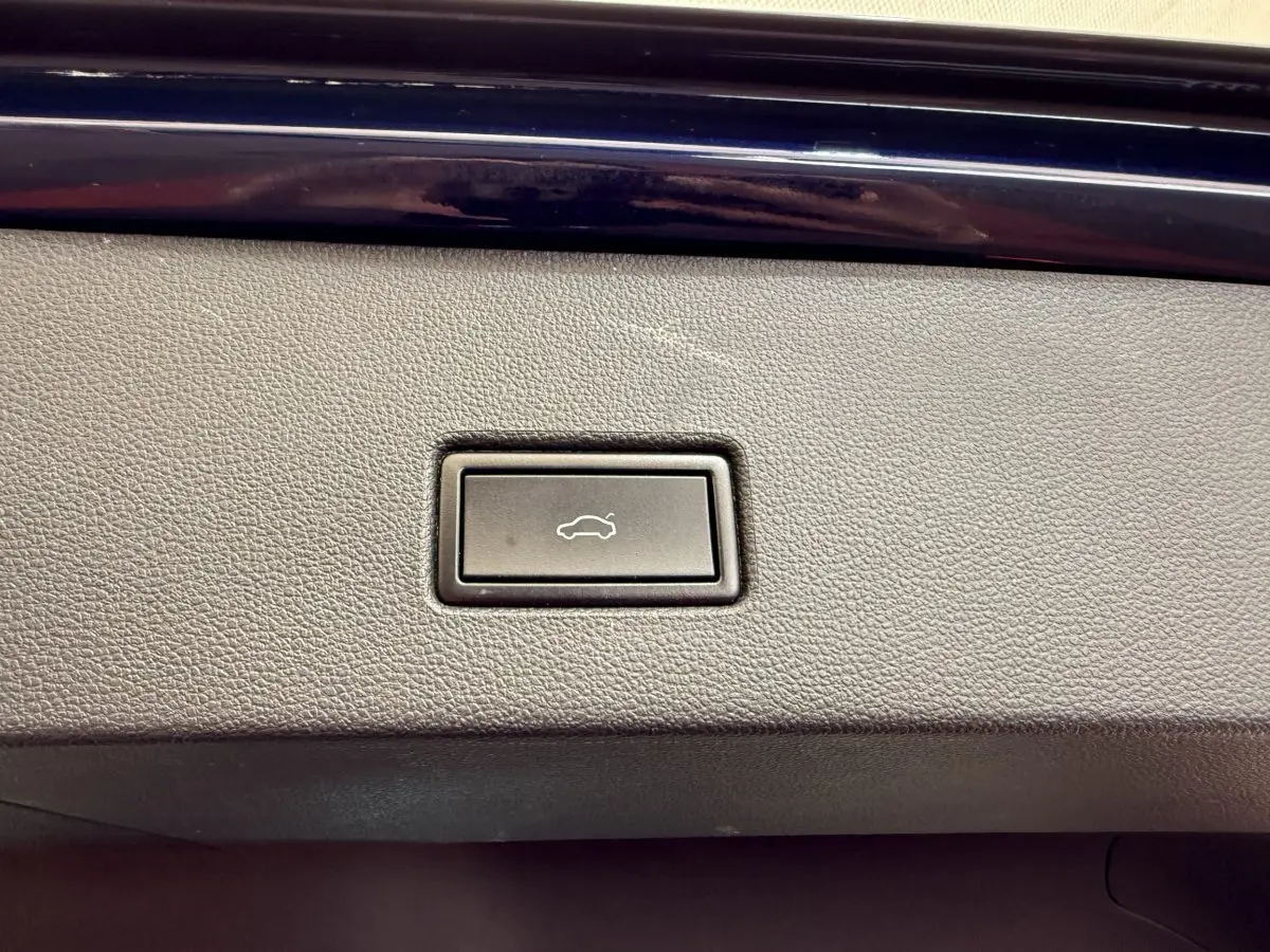 Bouton d'ouverture électrique du coffre sur la garniture intérieure grise d'un Volkswagen T-Roc bleu.