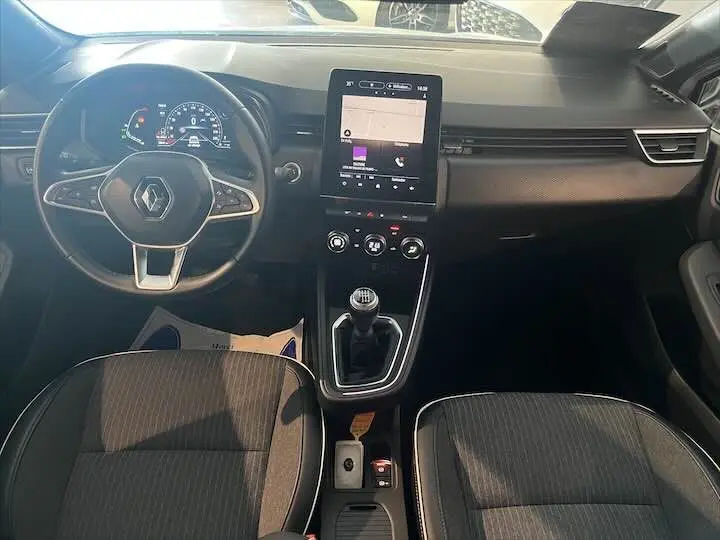 Vue intérieure frontale de la Renault Clio V 1.0 TCE avec tableau de bord moderne et levier de vitesse manuel.