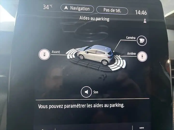 Affichage de l'aide au parking avec vue 3D d'une Renault Clio V blanche nacrée sur l'écran tactile du tableau de bord.