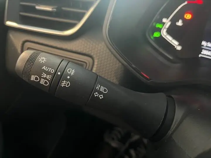 Gros plan sur la commande des phares et clignotants à gauche du volant dans une Renault Clio V blanche nacrée.