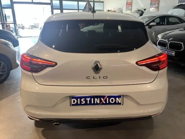Vue arrière d'une Renault Clio V blanche nacrée avec feux LED allumés dans un showroom.