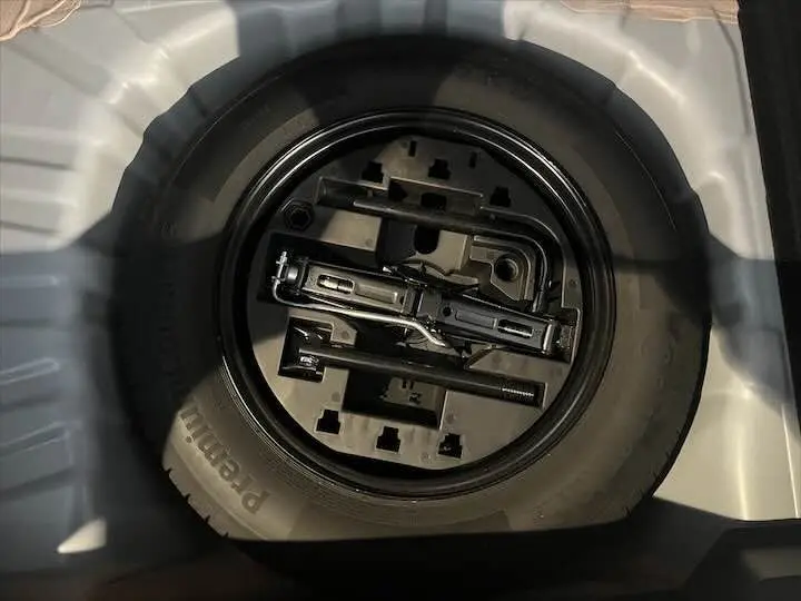 Gros plan sur la roue de secours et les outils de bord dans le coffre d'une Renault Clio V blanc nacré.