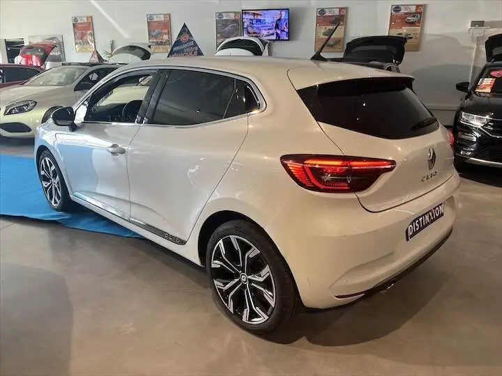 Renault Clio V blanc nacré vue 3/4 arrière droit en intérieur avec jantes alliage et vitres teintées.