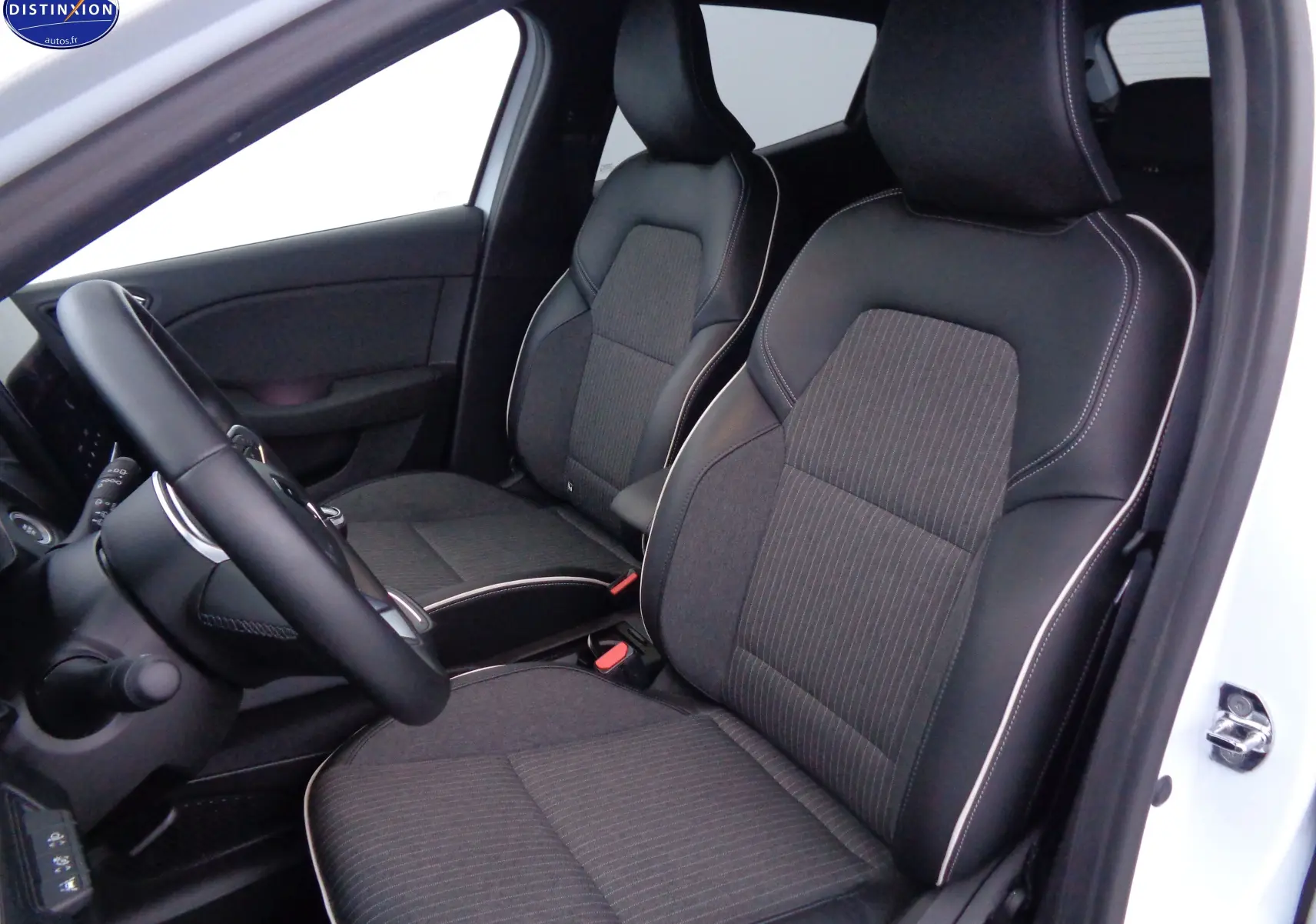 Vue intérieure côté conducteur de la Renault Clio V blanche nacrée, sièges en tissu gris et cuir noir avec surpiqûres blanches.