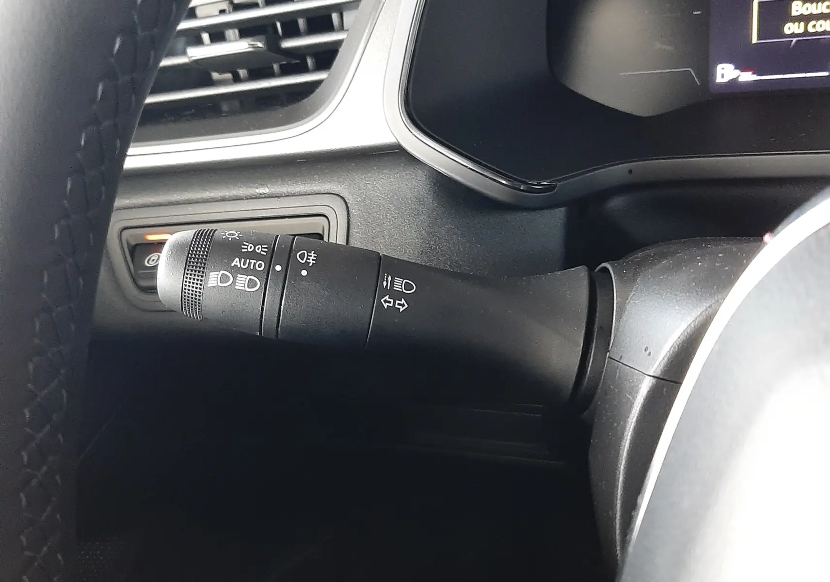 Gros plan sur la manette de commande des phares et clignotants à gauche du volant dans l'habitacle noir du Renault Captur E-Tech Hybrid 2024.