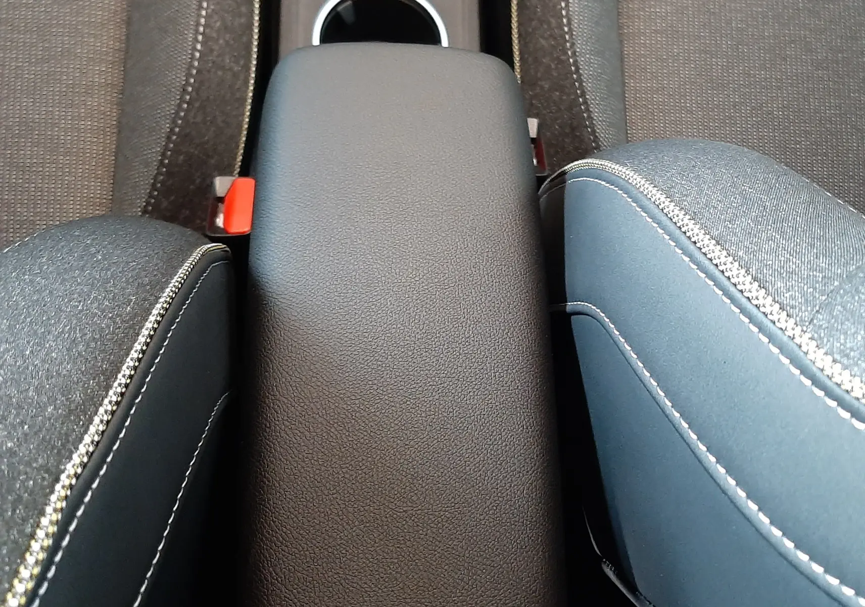 Vue plongeante sur l'accoudoir central noir entre les sièges en tissu gris et bleu du Renault Captur E-Tech Hybrid 2024.