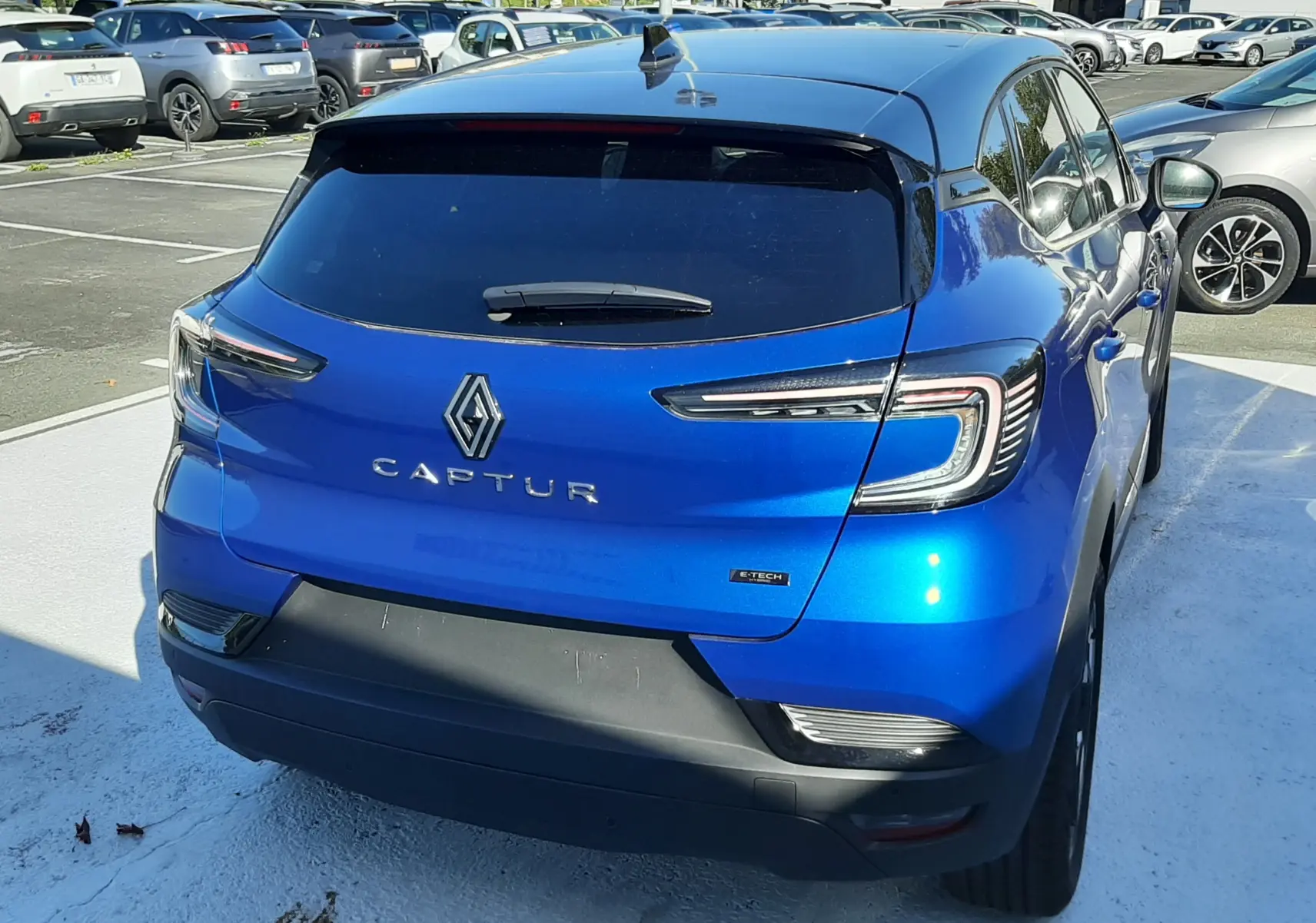 Vue 3/4 arrière droite du Renault Captur E-Tech Hybrid 145ch en bleu Iron avec toit noir, sur parking extérieur.