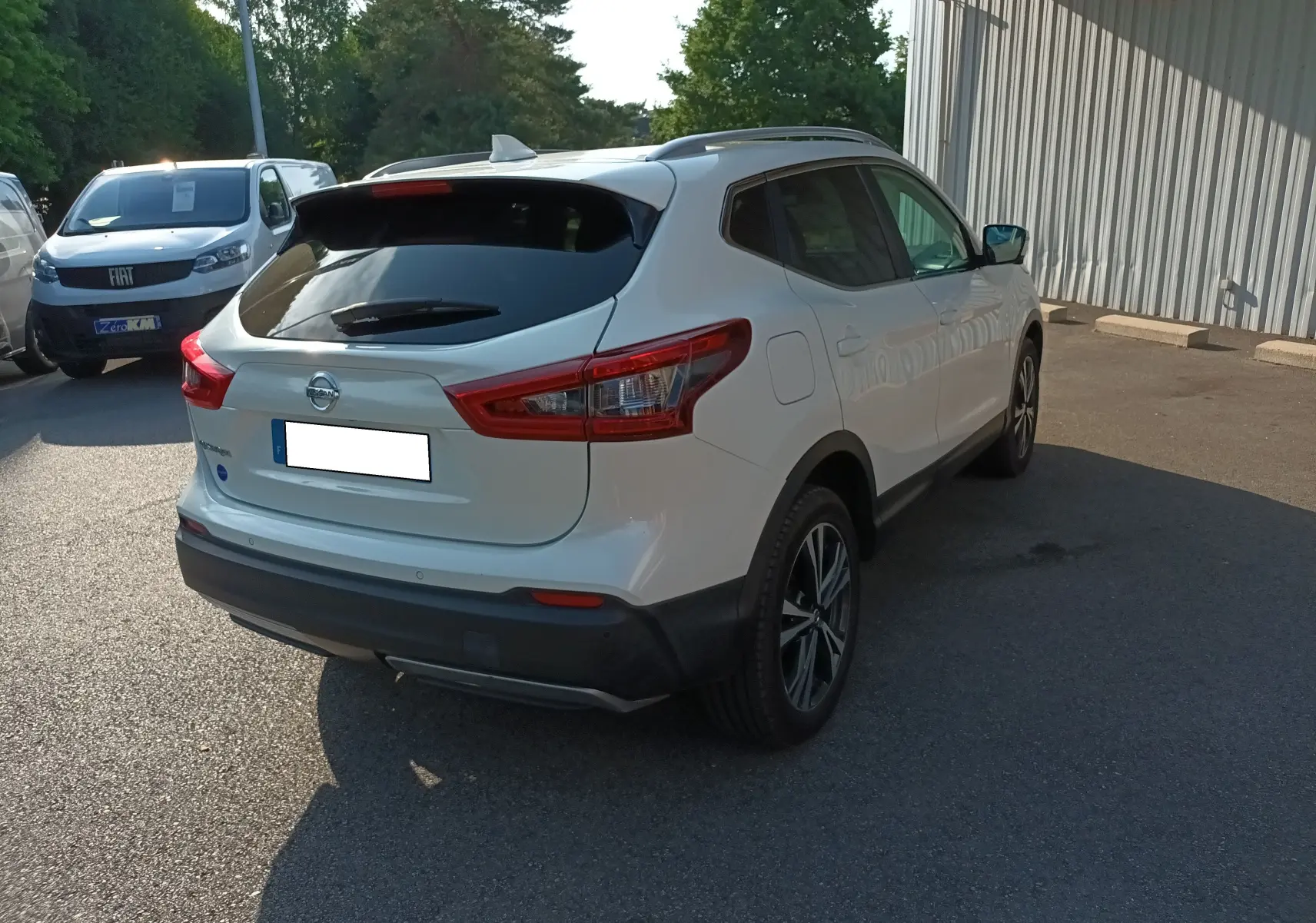 Nissan Qashqai blanc nacré vu de l'arrière droit, avec feux arrière LED et jantes alliage bicolores.