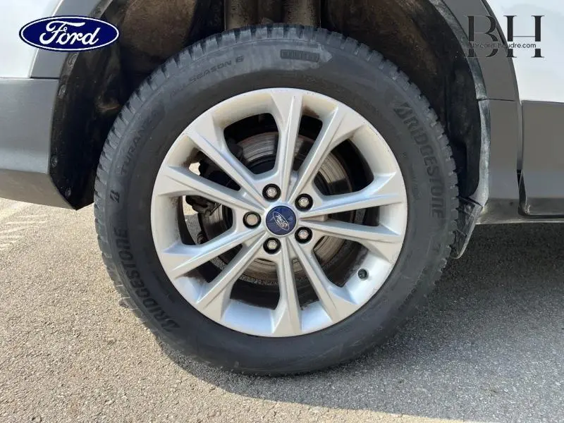 Gros plan sur la roue avant droite du Ford Kuga blanc Glacier, jante alliage et pneu Bridgestone visible