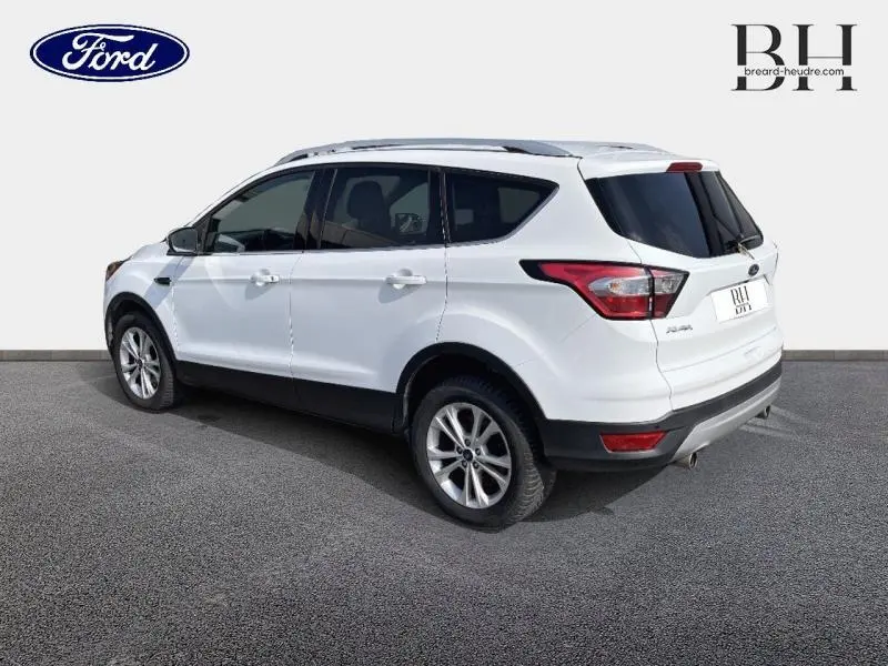 Ford Kuga blanc glacier vu en 3/4 arrière droit, avec barres de toit aluminium et hayon motorisé fermé.