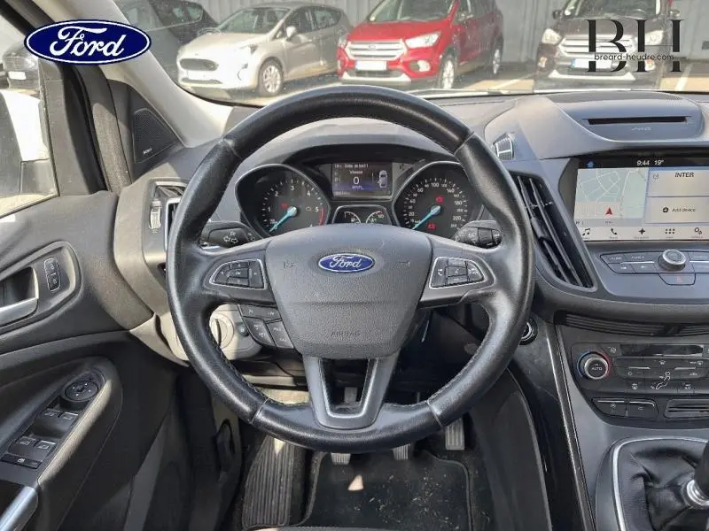 Vue centrée sur le volant cuir multifonction du Ford Kuga blanc Glacier, avec tableau de bord et écran GPS visible.