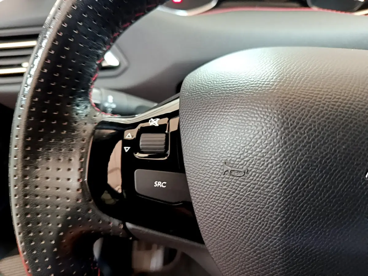 Gros plan sur le volant cuir perforé côté gauche du Peugeot 308 gris foncé, avec commandes audio intégrées.