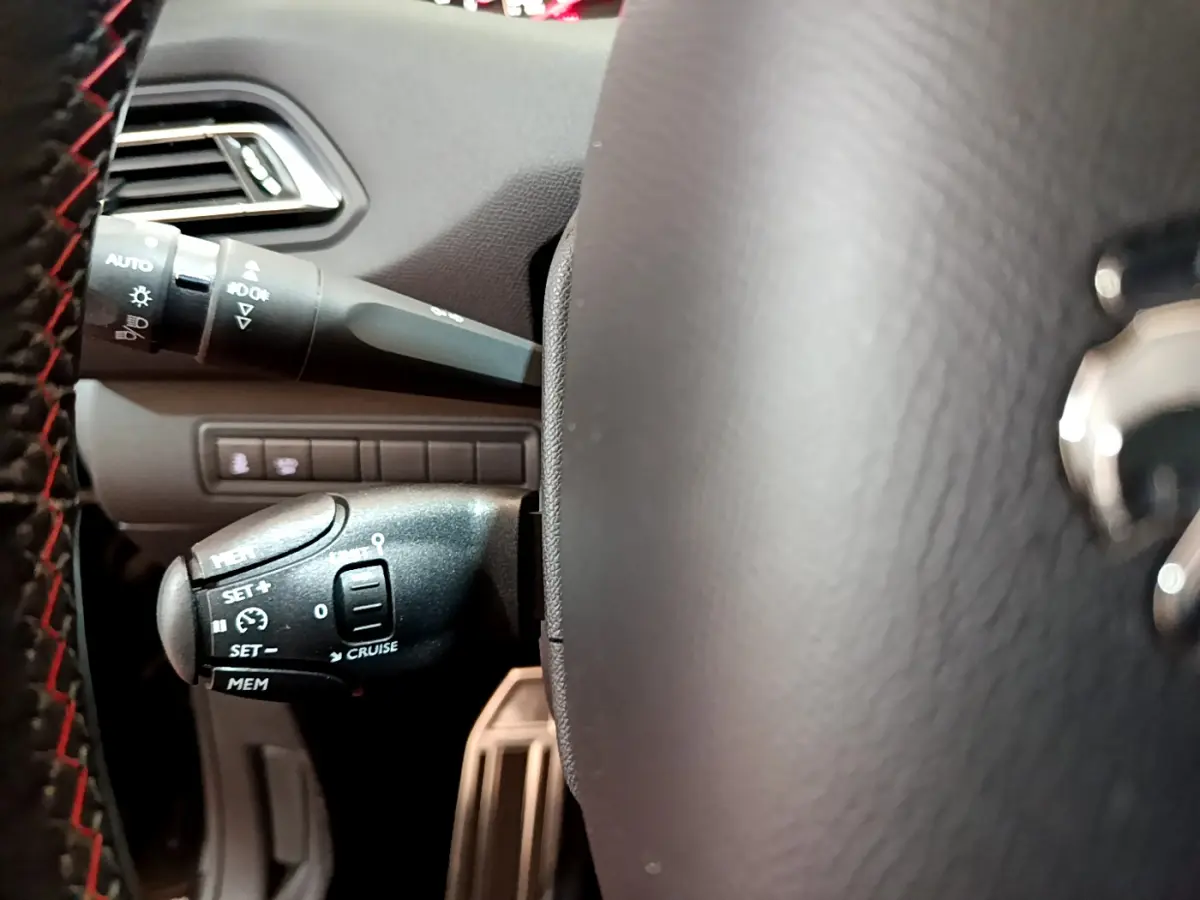 Gros plan sur la commande de régulateur de vitesse à gauche du volant cuir d'une Peugeot 308 gris foncé 2016.