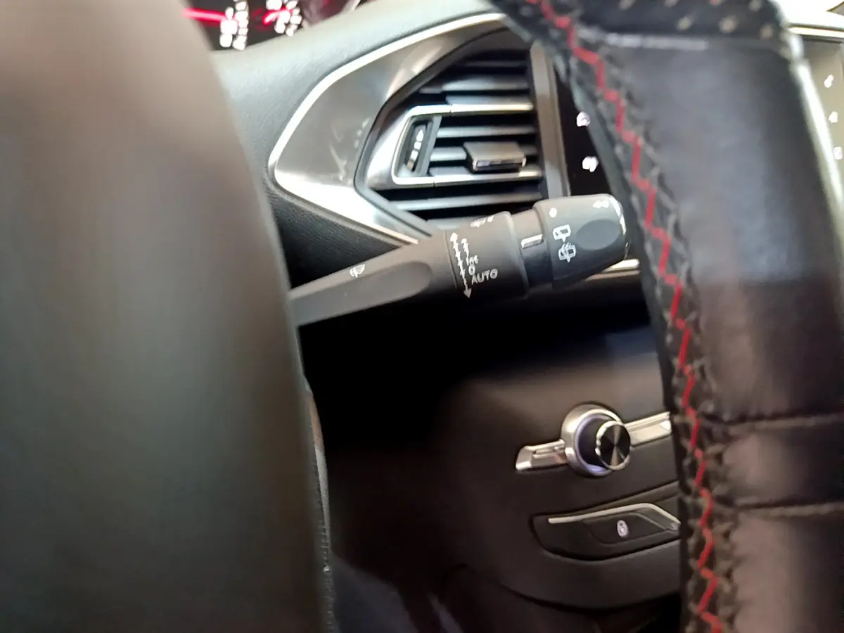 Gros plan sur la commande d'essuie-glace à gauche du volant cuir avec surpiqûres rouges dans l'habitacle gris foncé Peugeot 308.