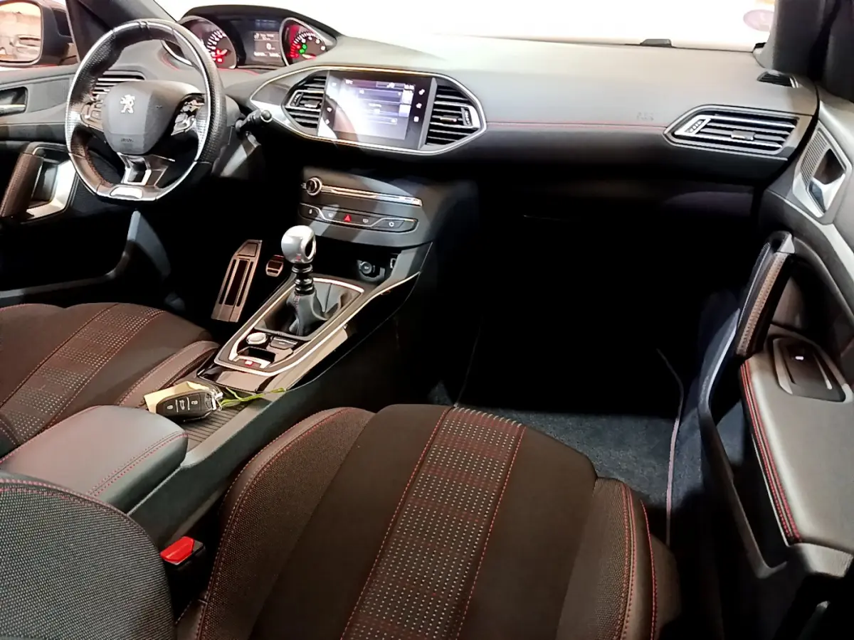 Intérieur Peugeot 308 GT Line 2016 vu côté passager, volant cuir, écran tactile et sellerie noire avec surpiqûres rouges.