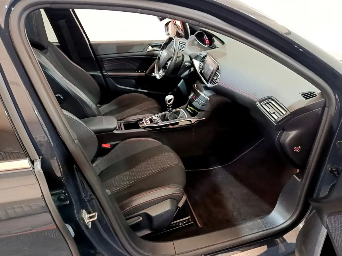Intérieur avant droit d'une Peugeot 308 gris foncé, avec tableau de bord moderne et levier de vitesse manuel visible.