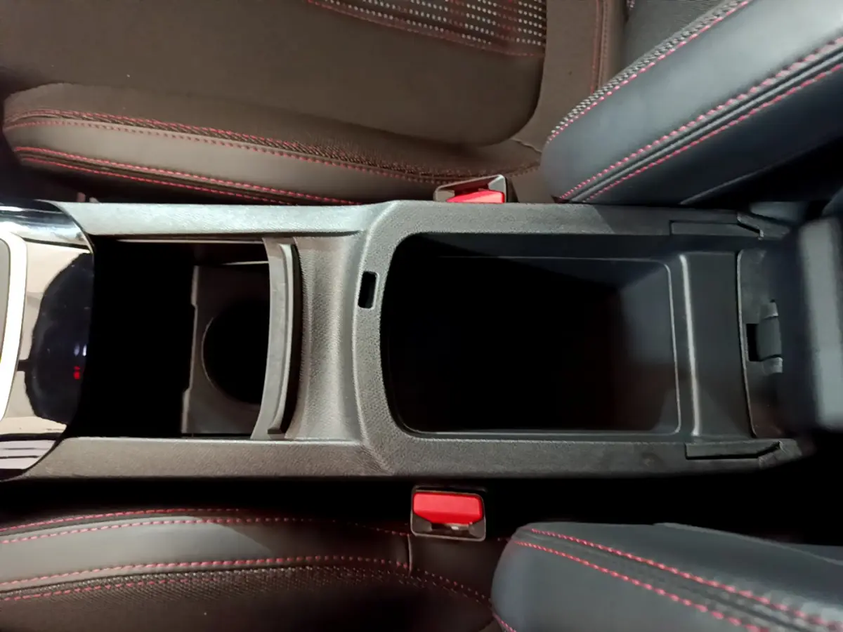 Vue plongeante sur la console centrale noire avec rangement ouvert et sièges tissu gris foncé à surpiqûres rouges du Peugeot 308 GT Line.