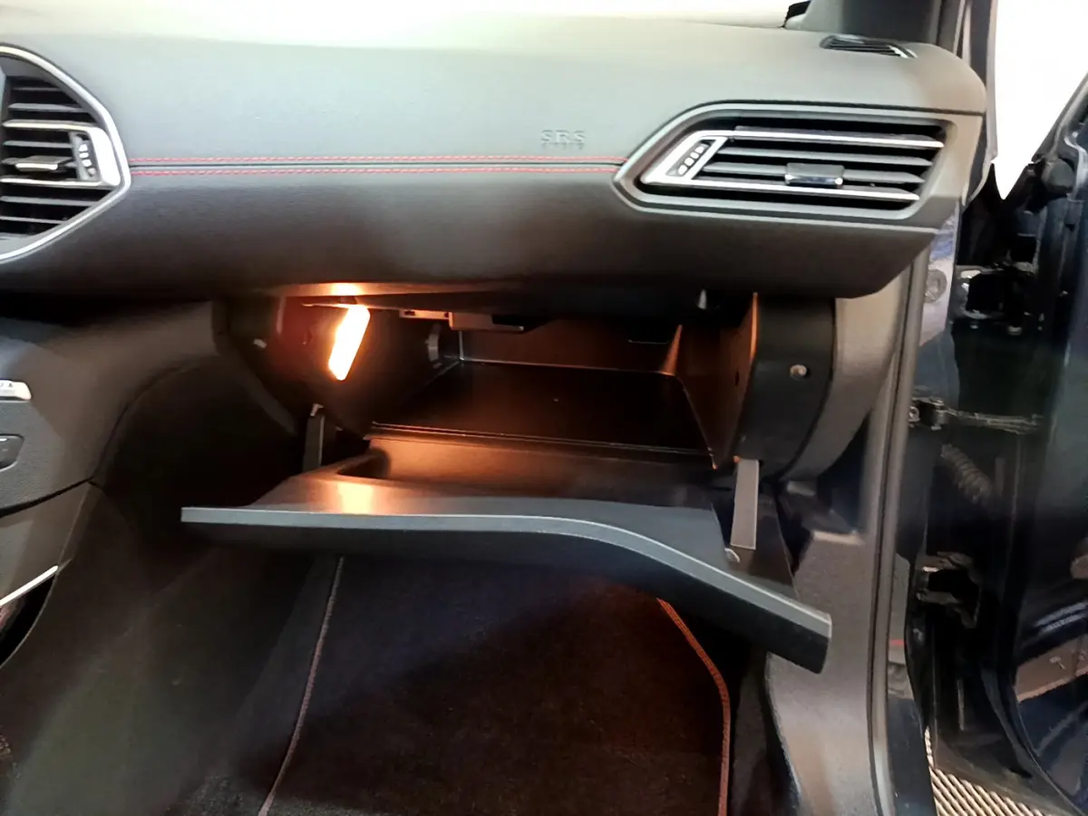 Boîte à gants ouverte éclairée côté passager d’une Peugeot 308 gris foncé, intérieur noir avec surpiqûres rouges.