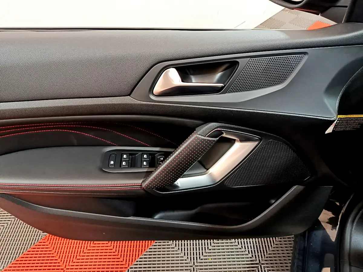 Poignée de porte côté gauche avec surpiqûres rouges et commandes des vitres dans l'habitacle d'une Peugeot 308 GT Line 2016.