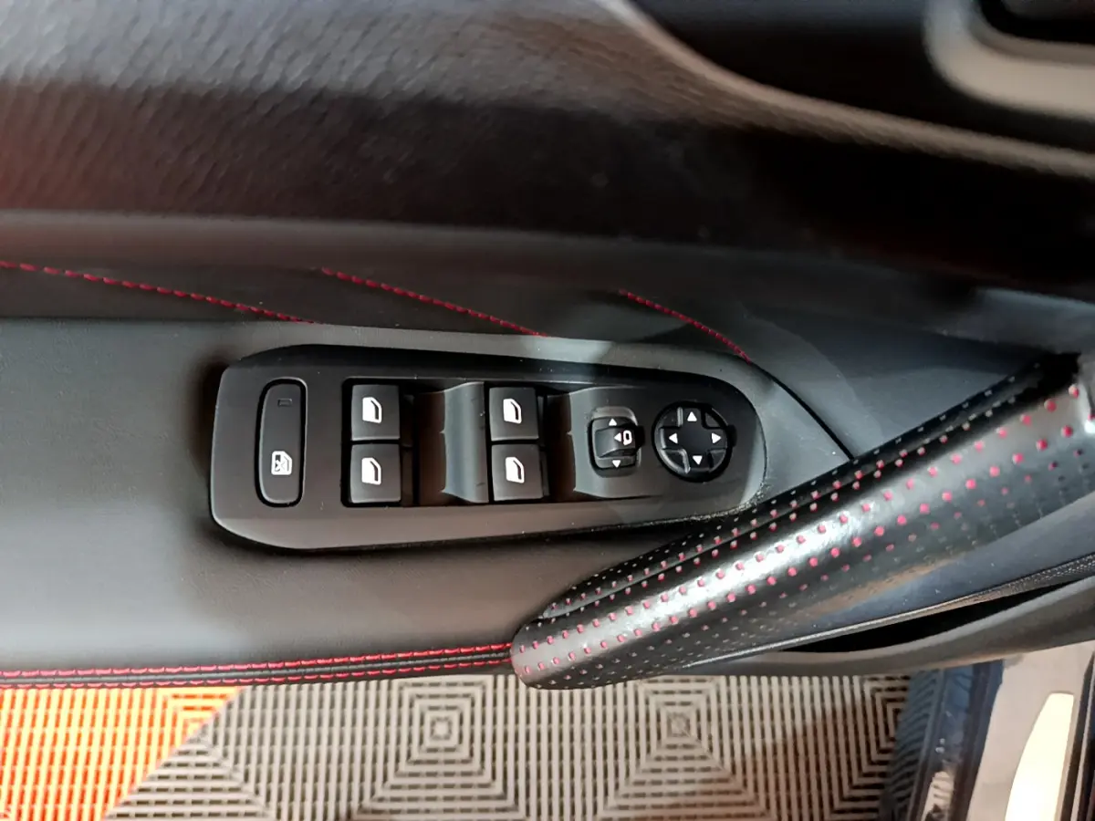 Gros plan sur la commande des vitres et rétroviseurs côté conducteur du Peugeot 308 gris foncé avec surpiqûres rouges.