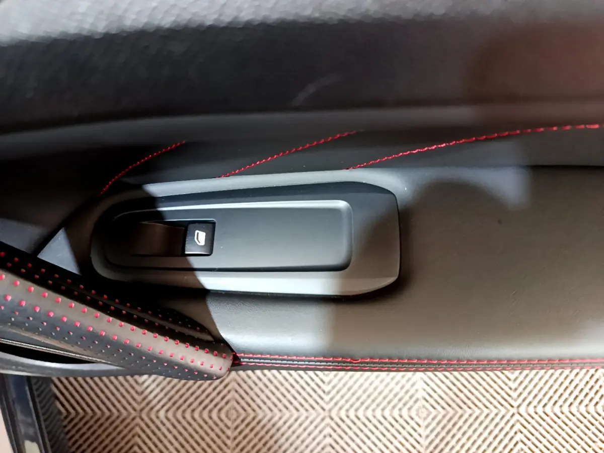 Bouton de lève-vitre électrique sur la porte côté gauche du Peugeot 308 gris foncé avec surpiqûres rouges.