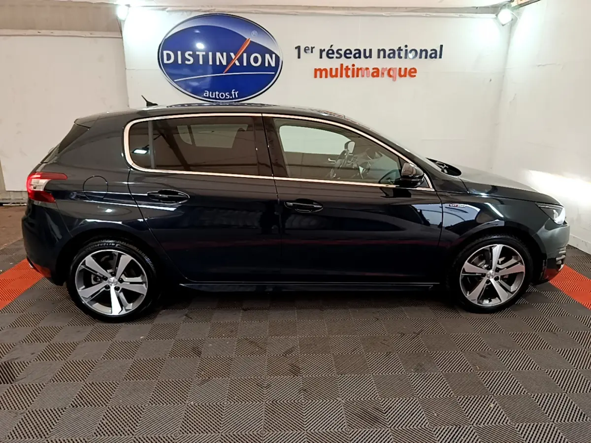 Profil côté gauche d'une Peugeot 308 gris foncé 2016 GT Line avec jantes alliage et vitres teintées en intérieur showroom.