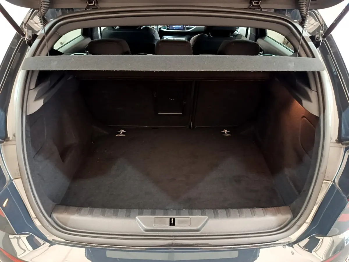 Coffre ouvert vu de l'arrière d'une Peugeot 308 gris foncé, montrant l'espace de chargement vide et la tablette de séparation.
